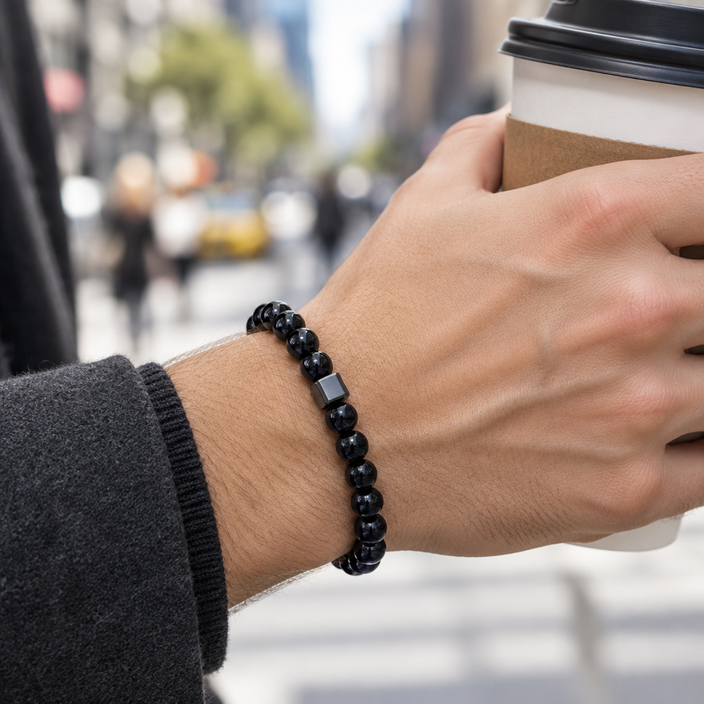 Lifestyle – ulica: nadgarstek z bransoletką z czarnych koralików 8 mm trzymający kawę na tle miejskiej ulicy